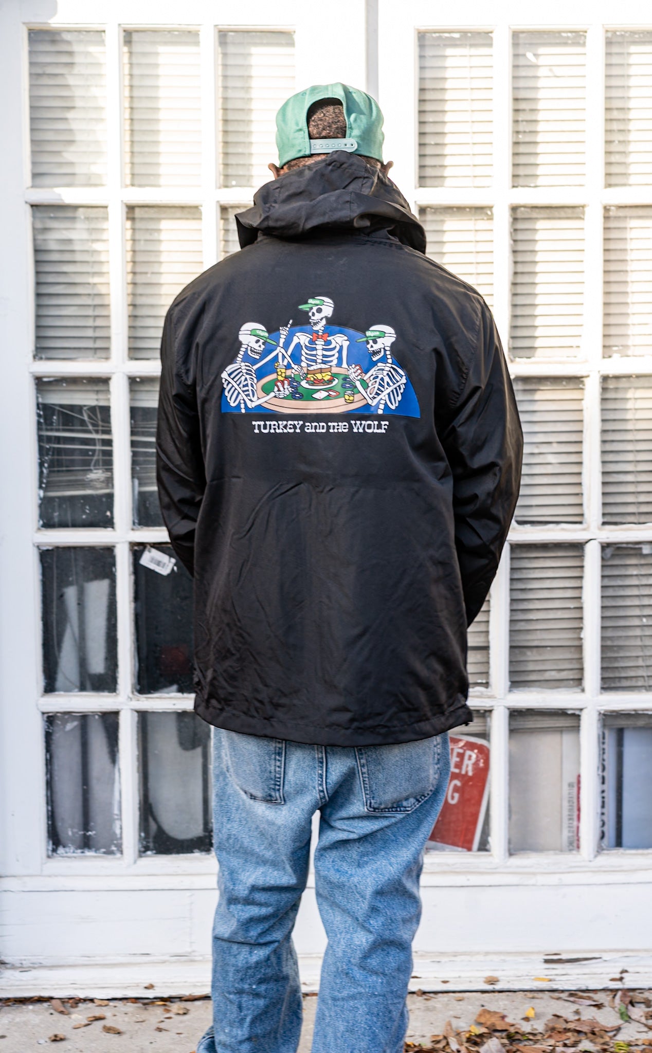 Person wearing a black jacket with a colorful design on the back, standing in front of a windowed door.