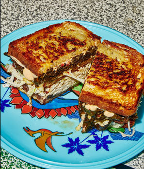 Grilled sandwich with golden-brown crust, filled with meat and coleslaw, on a blue patterned plate.