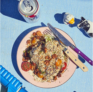 A plate of food with utensils, a soda can, and toys on a blue picnic table under sunlight.