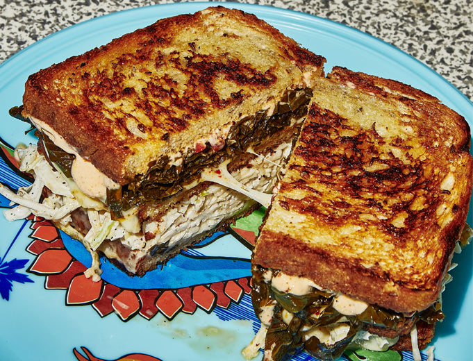 Grilled sandwich with golden-brown crust, filled with meat and coleslaw, on a blue patterned plate.
