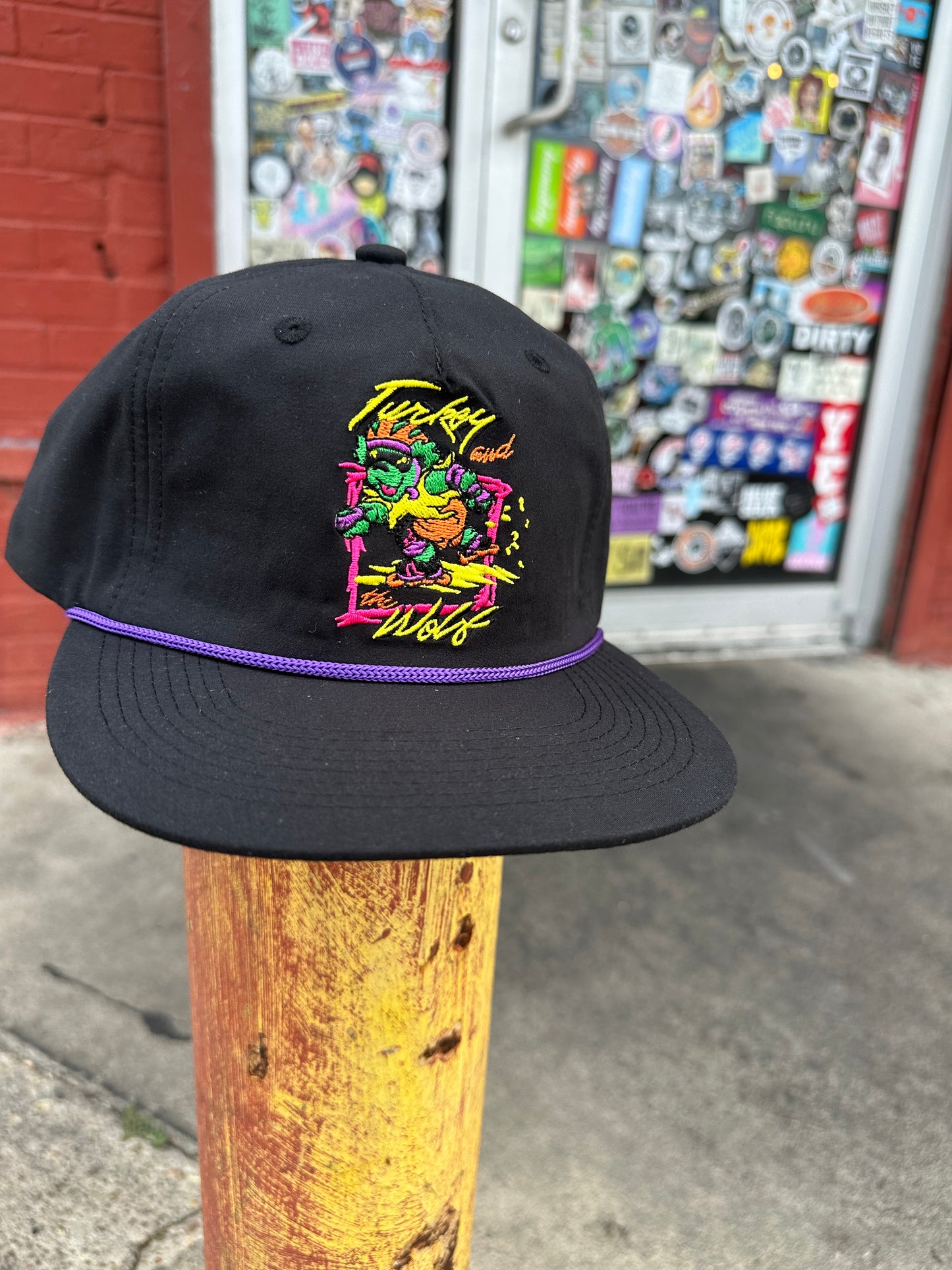 black hat with purple cord that has embroidery that says turkey and the wold and a rollerblading bear