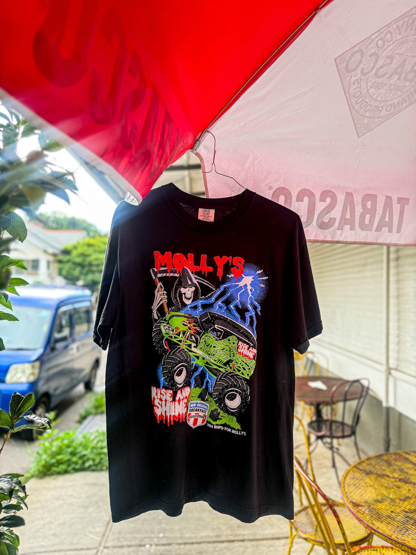 Black t-shirt with colorful graphic design held by a person outdoors under an umbrella