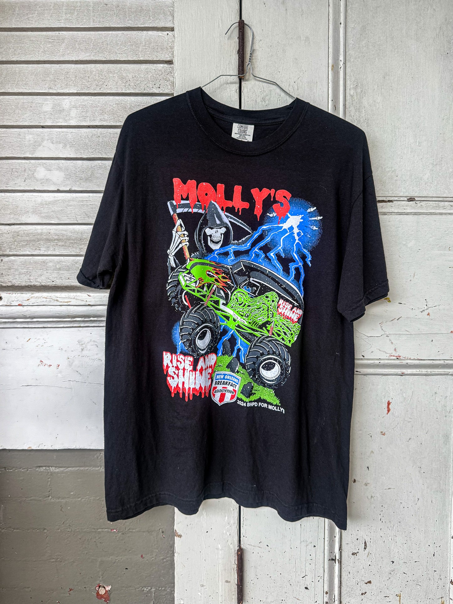 Black t-shirt with colorful graphic design hanging on a white wall.