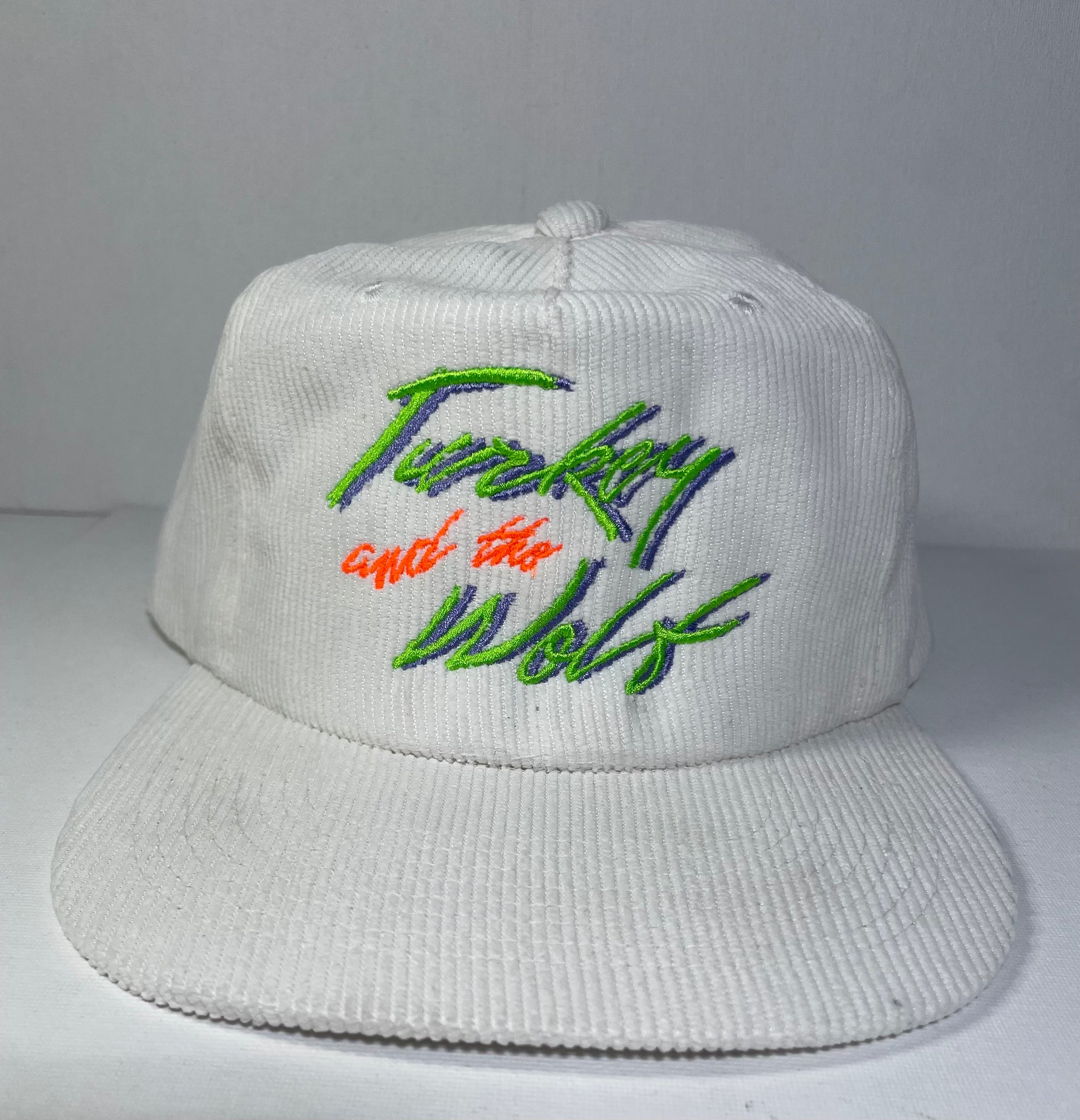 White corduroy hat that says turkey and the wolf in green and blue text