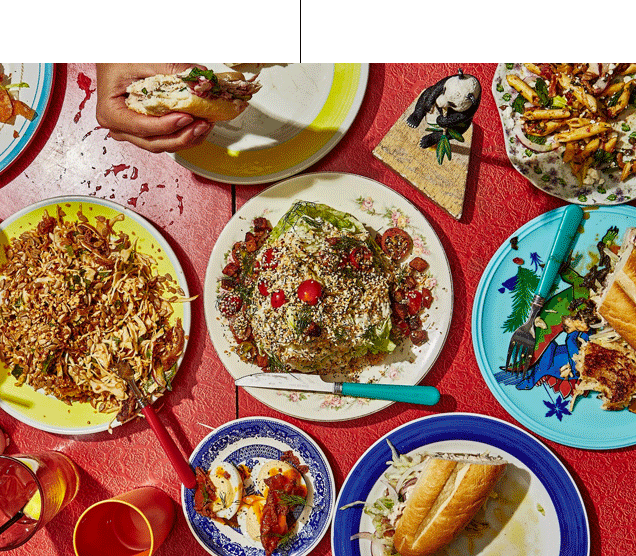 An array of eclectic dishes on a red textured tablecloth, with hands holding a sandwich, in bright sunlight.
