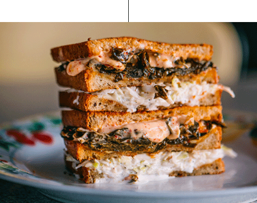 A hearty toasted sandwich with layers of filling on a decorative plate, captured in a close-up view.