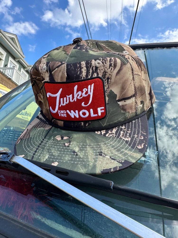 A camouflage Turkey and the Wolf cap placed on a car's rear windshield in a sunny outdoor setting.