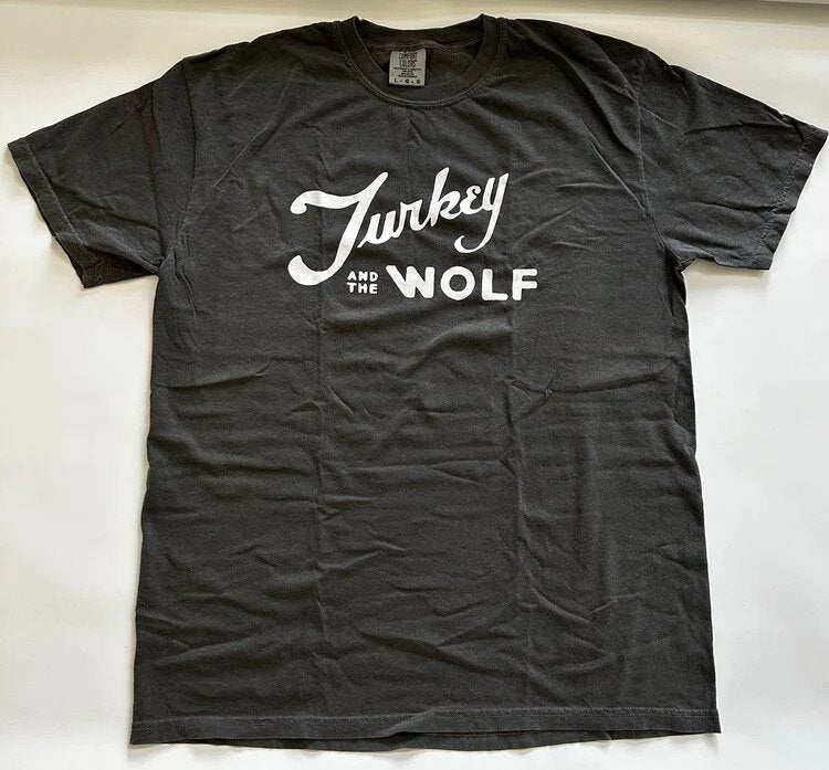 A charcoal gray t-shirt with Turkey and the Wolf in white cursive lettering, spread on a light background.