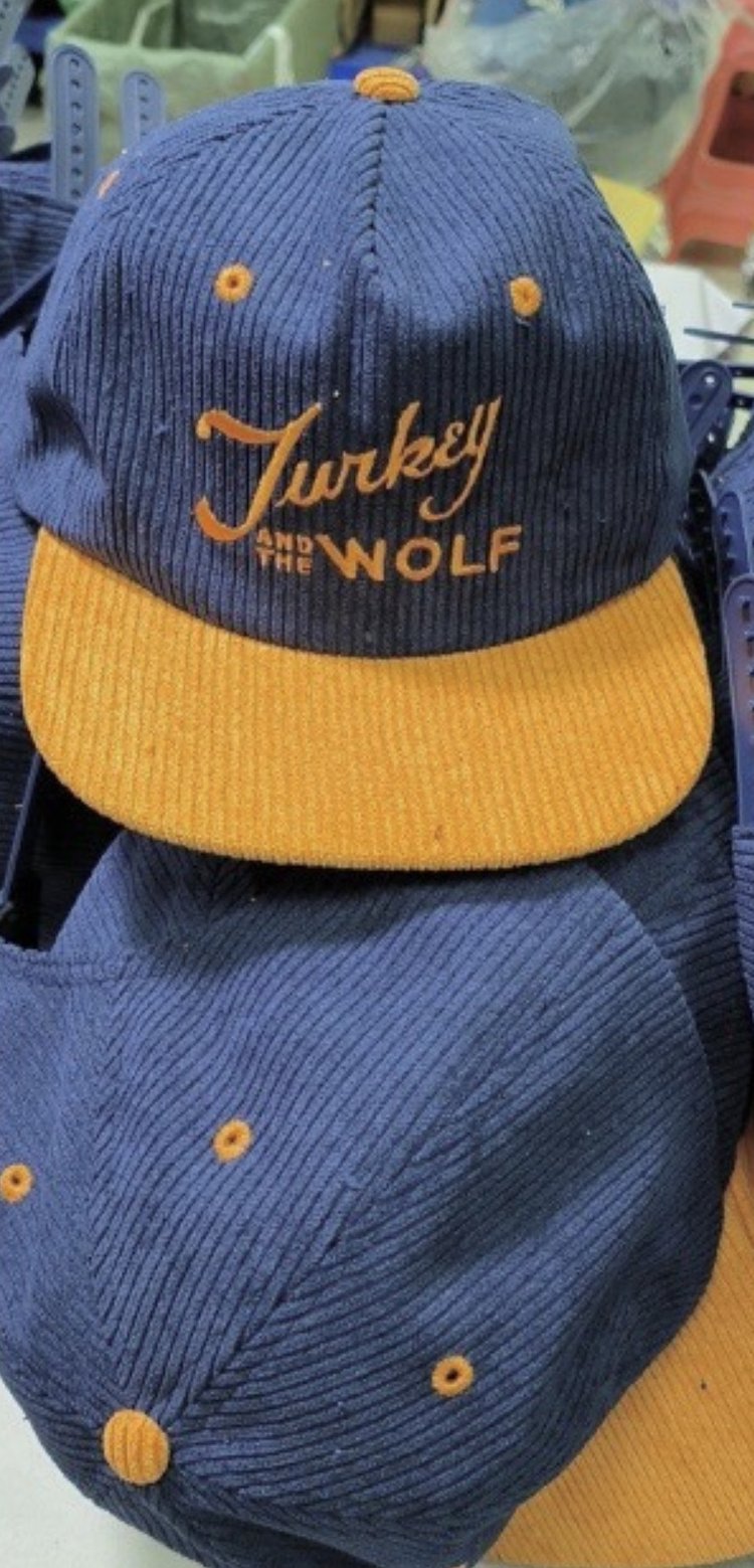 A navy and orange Turkey and the Wolf branded baseball cap displayed on a rack.