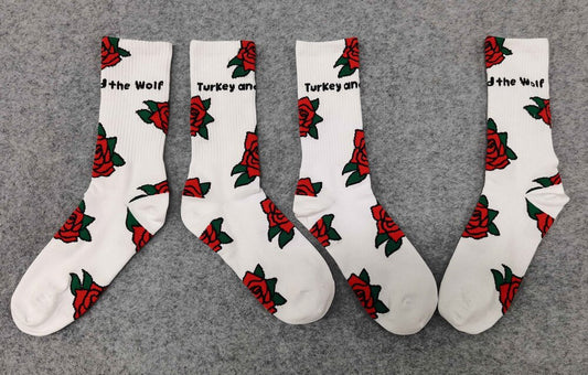 Two pairs of white socks with Turkey and the Wolf text and red rose patterns displayed on a grey background.
