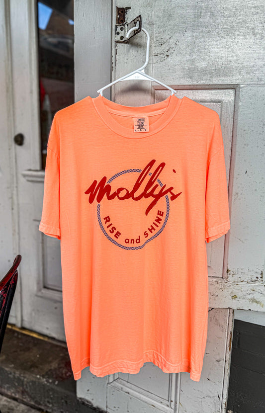 Orange t-shirt with 'Molly Rise and Shine' text on a hanger against a wooden door background