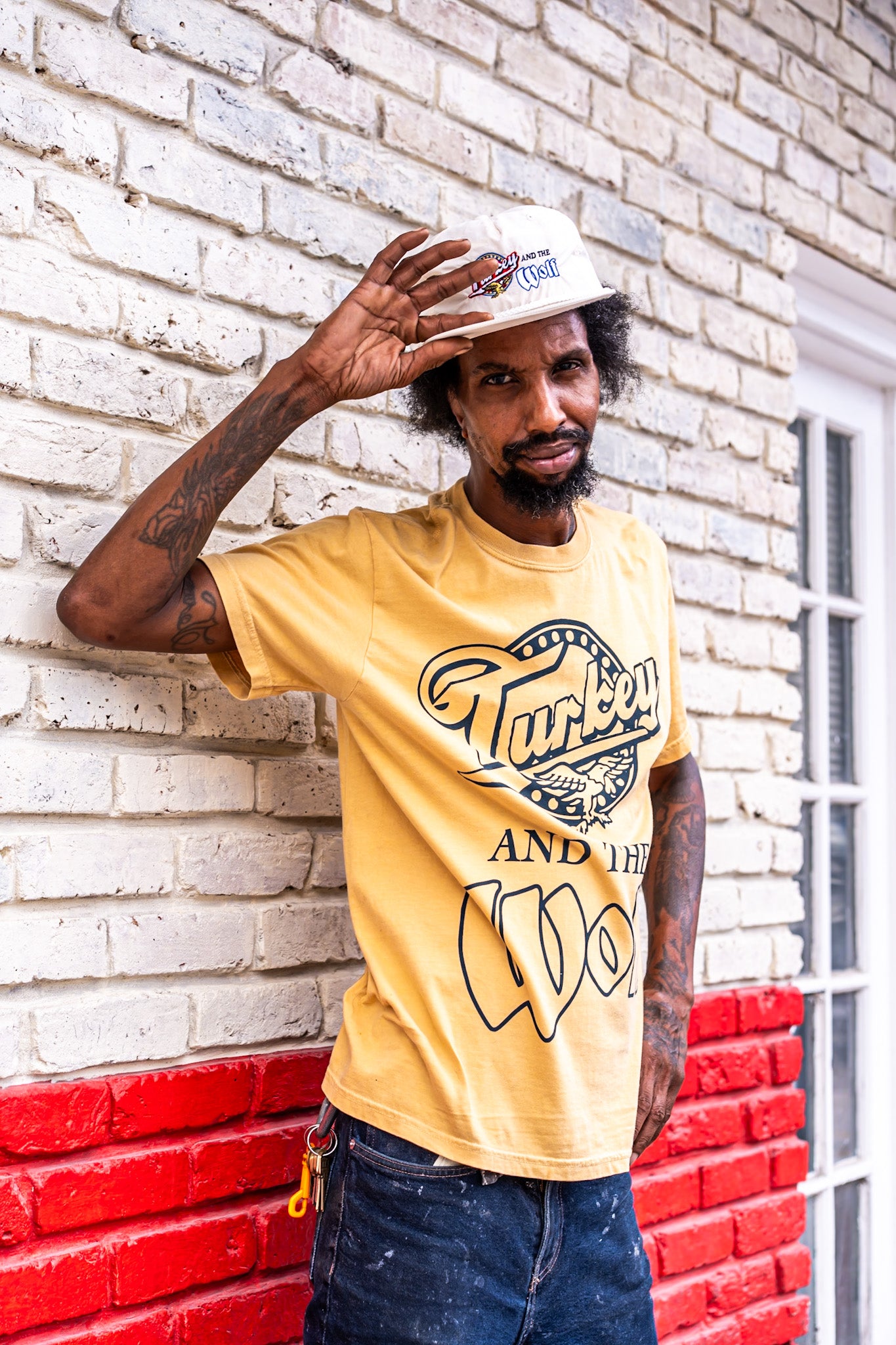 Man wearing a yellow t-shirt with graphic design, standing against a brick wall.