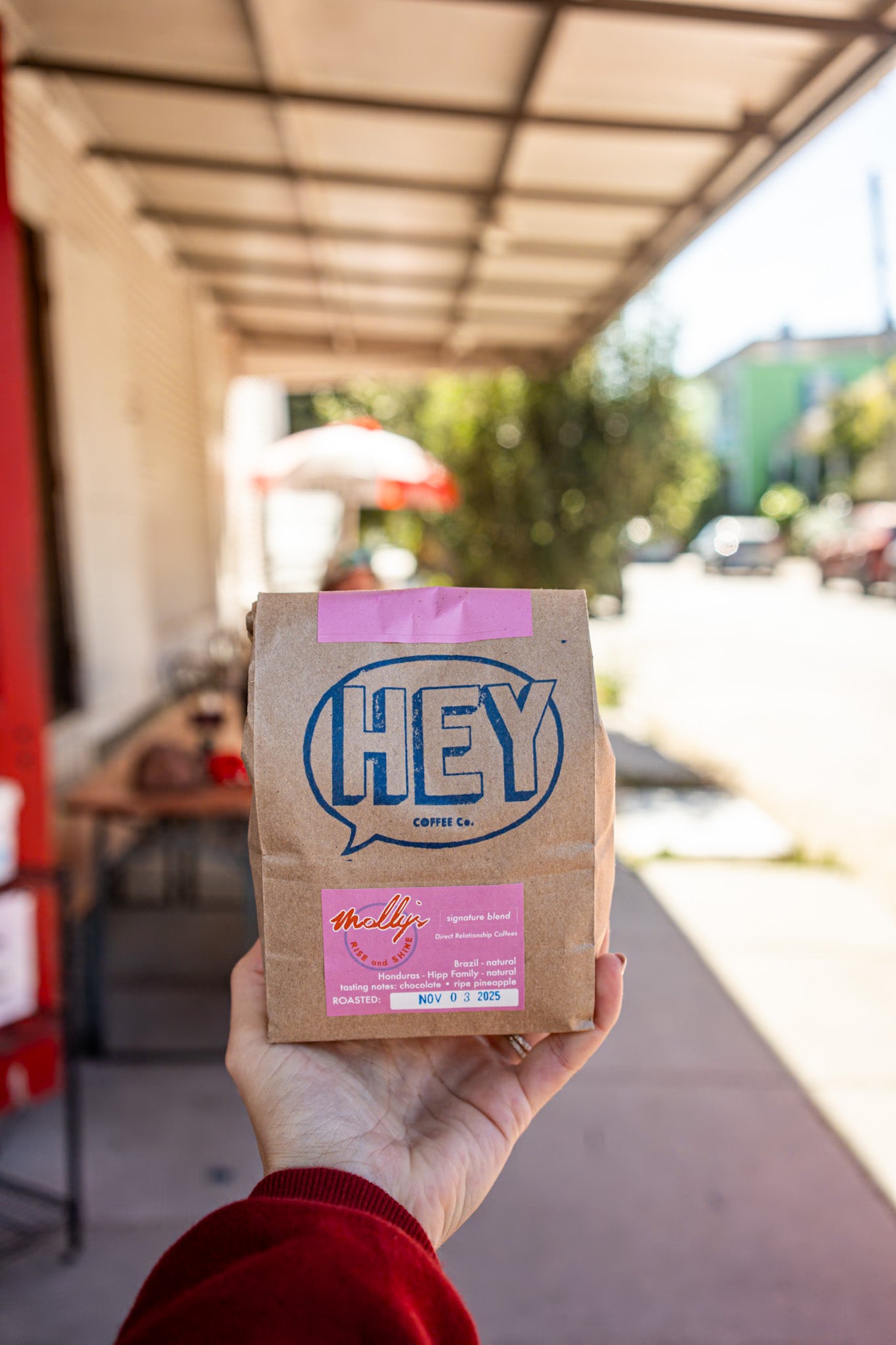 Hand holding a 'HEY' coffee package outdoors