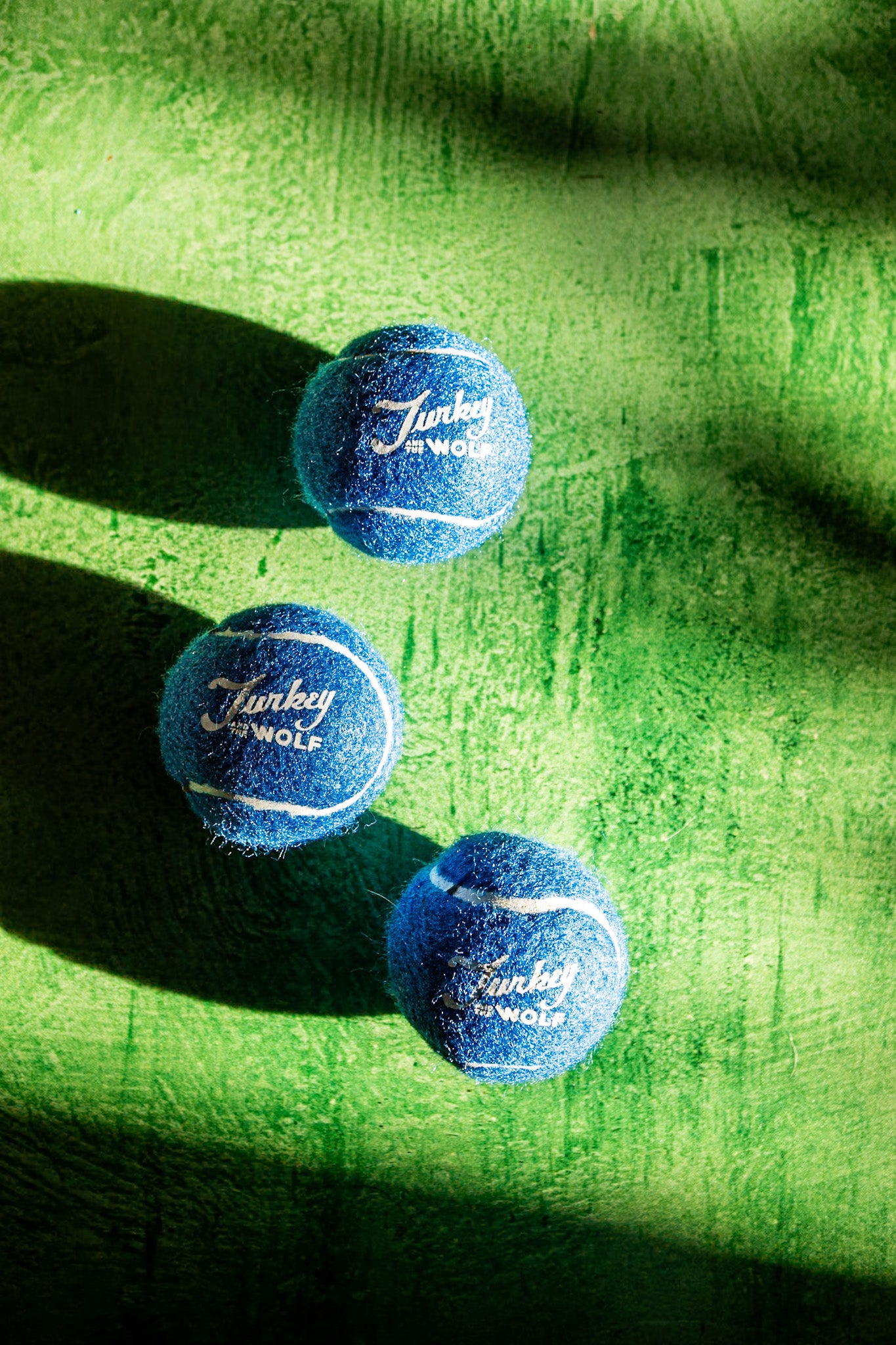 Three blue tennis balls with branding on a green surface