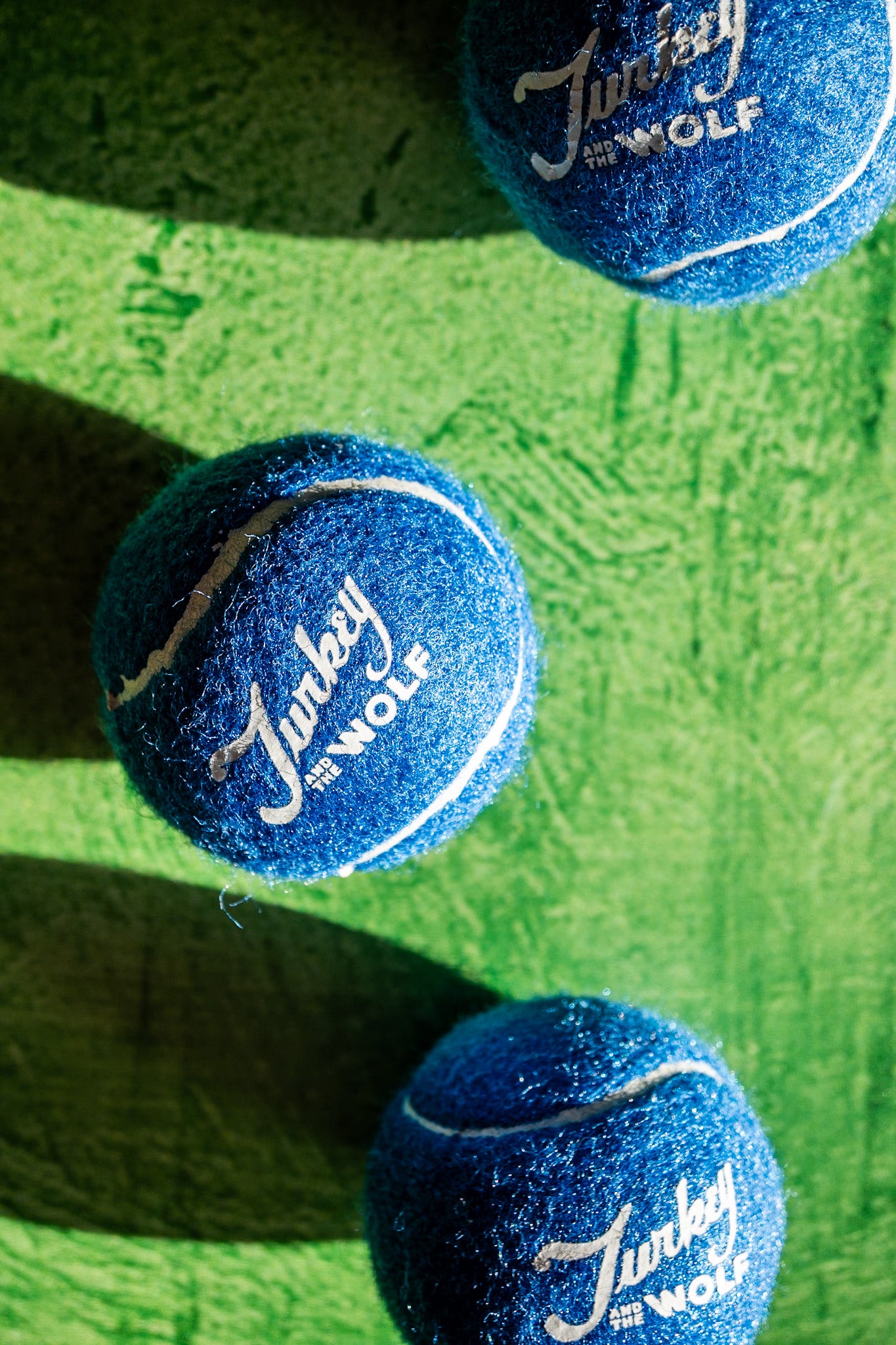 Three blue tennis balls with 'Turkey by Wolf' branding on a green surface.