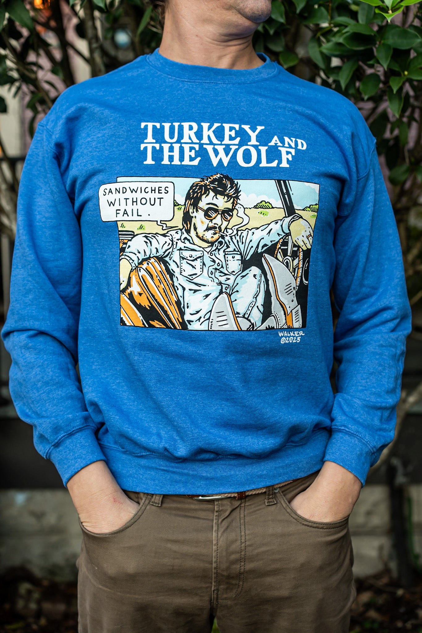 Person wearing a blue sweatshirt with a graphic design and text, standing against a natural background.