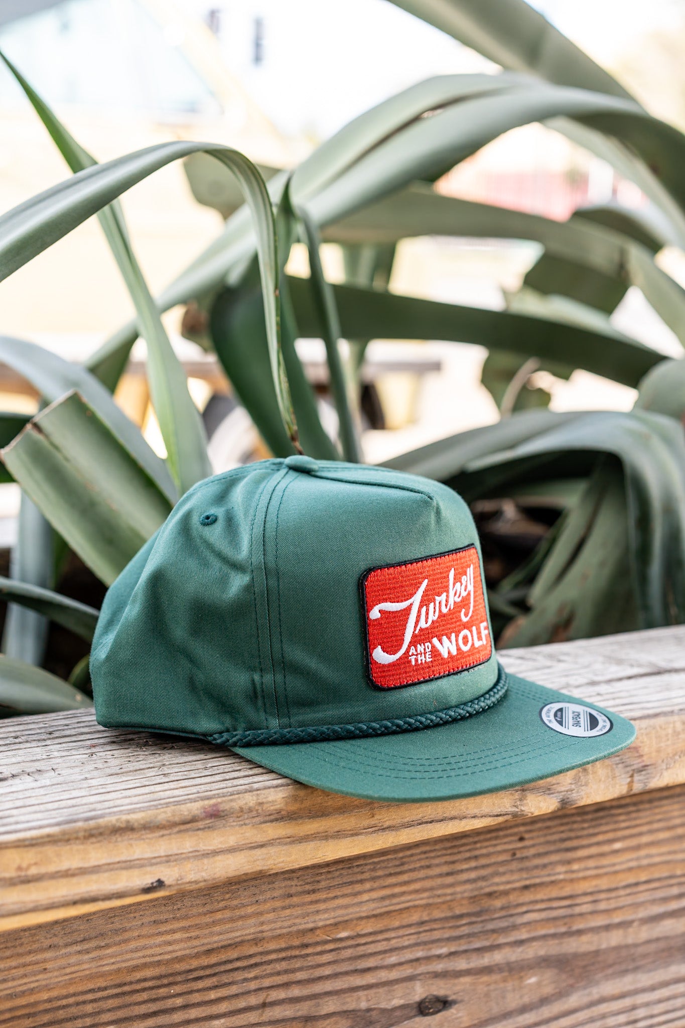 Green cap with a red logo on a wooden surface with plants in the background