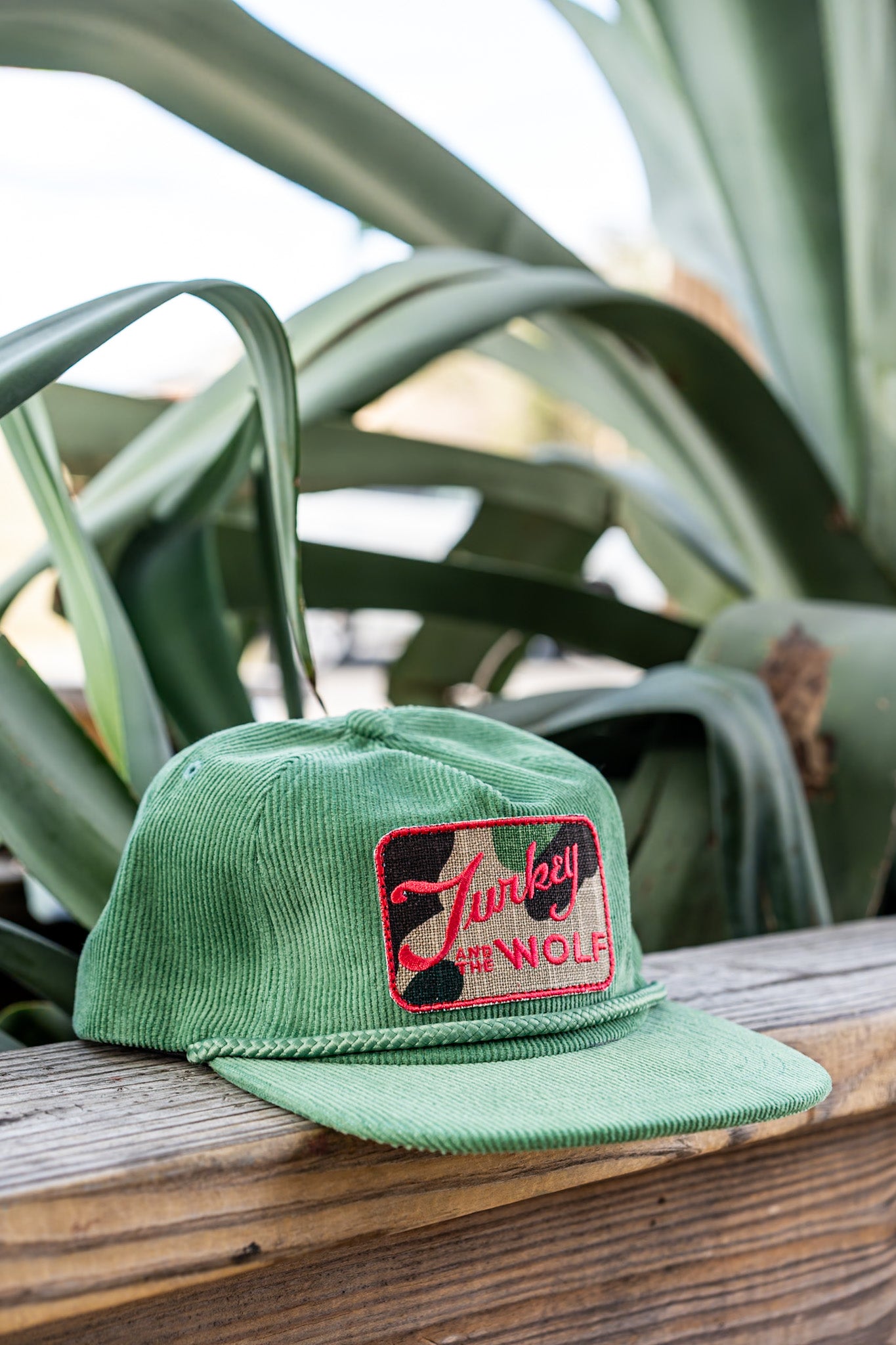 Green cap with a logo on a wooden surface with plants in the background