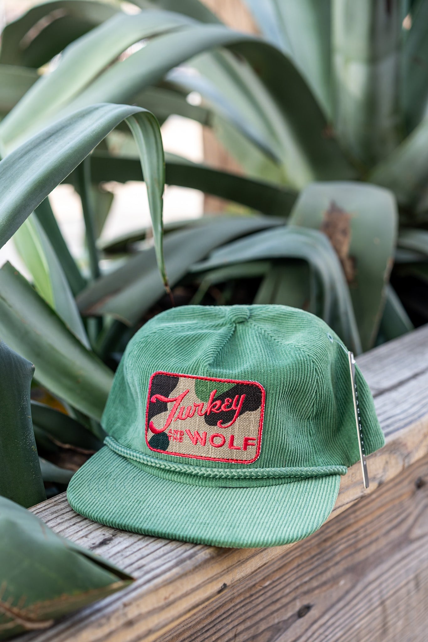 Green cap with a logo on a wooden surface with plants in the background