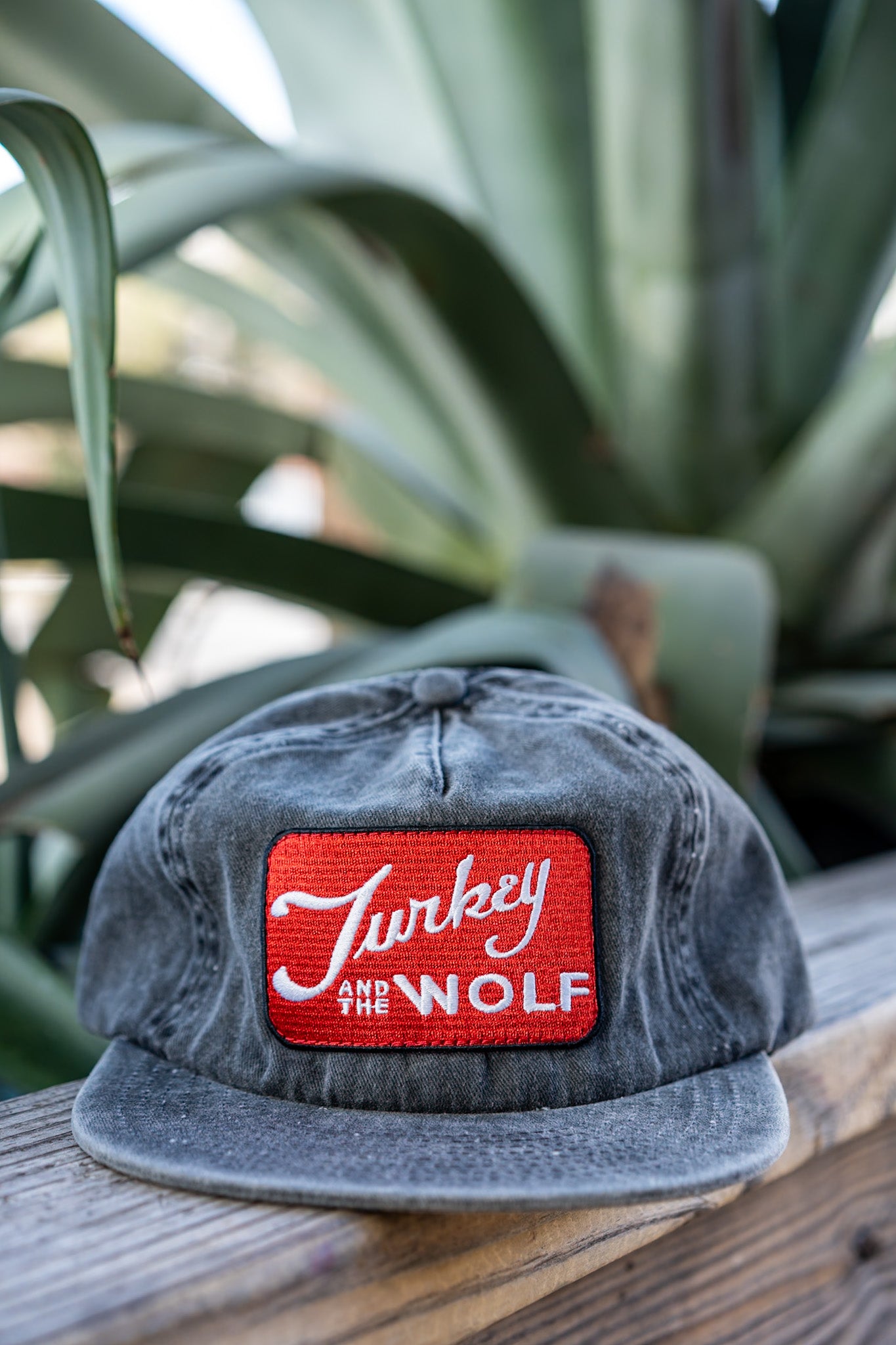 Gray cap with a red and white logo on a wooden surface with green plants in the background