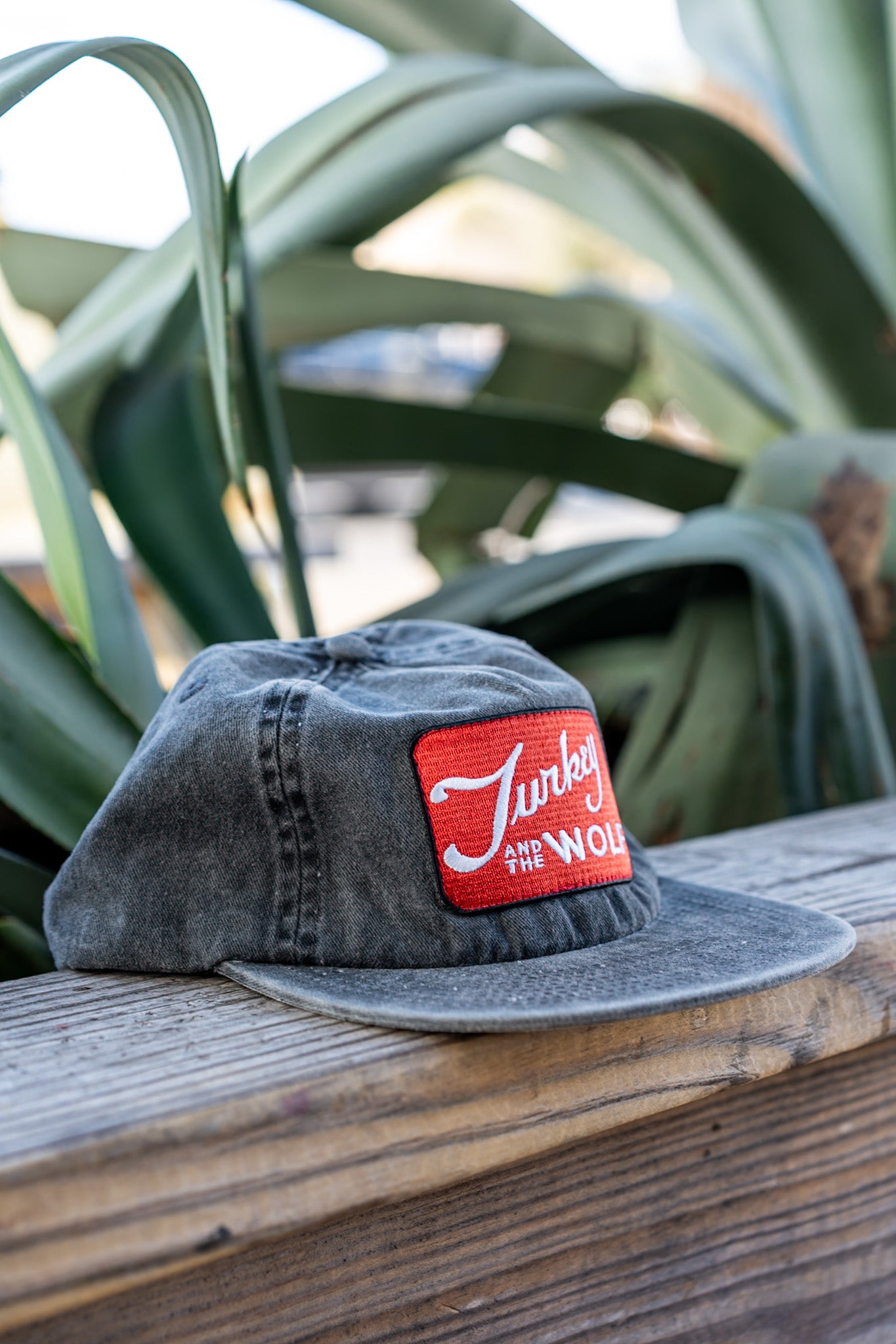 Gray cap with a red and white logo on a wooden surface with green plants in the background