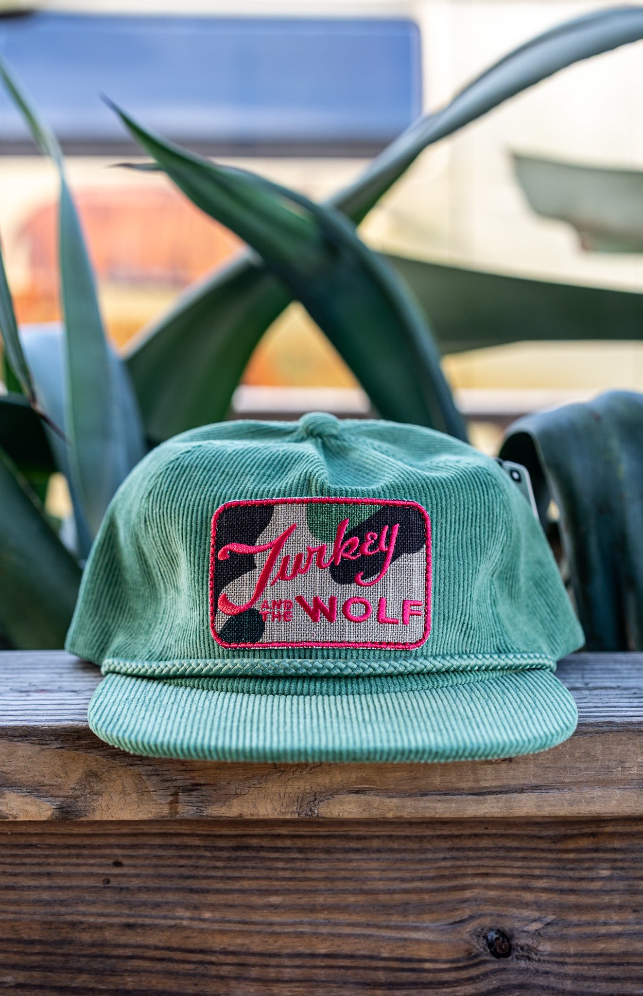 Green cap with pink logo on a wooden surface with blurred background