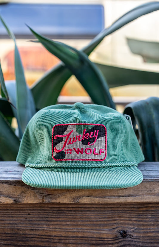 Green cap with pink logo on a wooden surface with blurred background