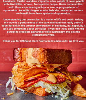 A close-up of a stacked sandwich with crispy bacon, chips, cheese, and sauce on a slate surface
