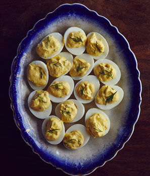 A plate of deviled eggs garnished with herbs on a dark wood surface, shot from above.