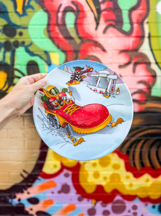 Person holding a plate with a colorful illustration of a red shoe against a vibrant, abstract mural background.