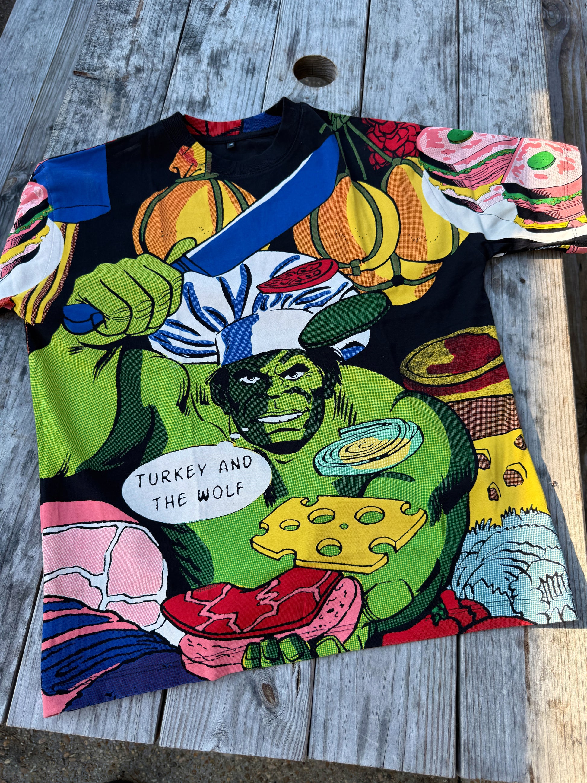 Colorful t-shirt with graphic design of a character holding a turkey and text on a wooden surface