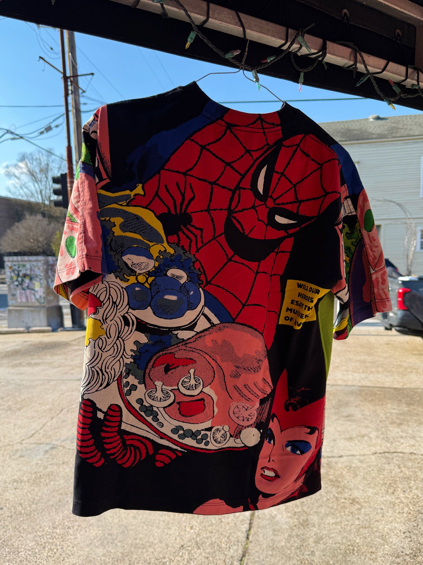 Colorful superhero-themed shirt hanging outdoors on a clothesline.