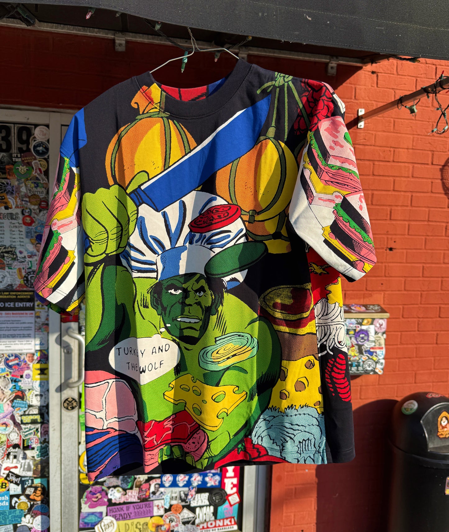 Colorful graphic t-shirt with superhero design hanging against a red brick wall.
