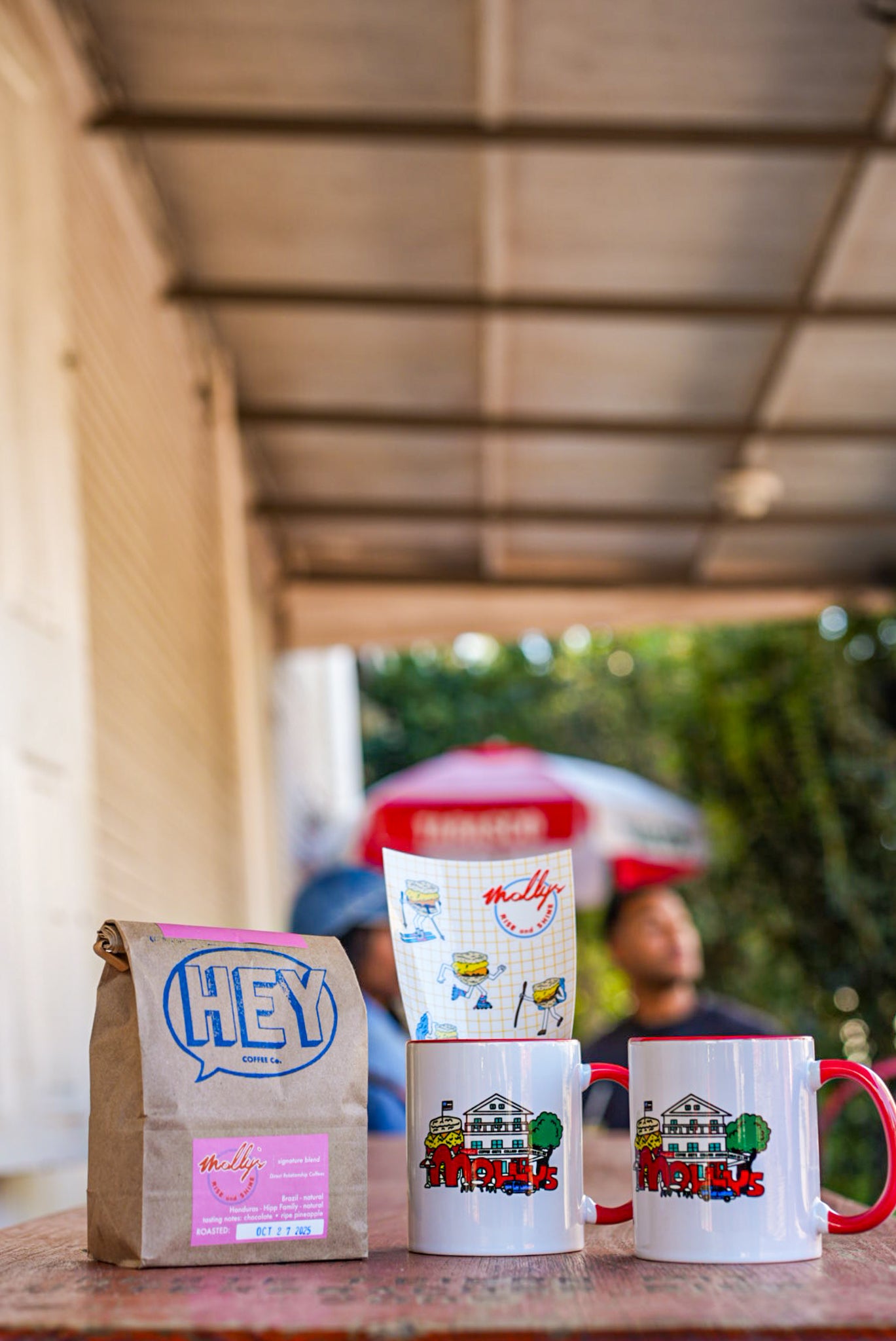 Three mugs with colorful designs and a coffee bag on a table with a blurred background
