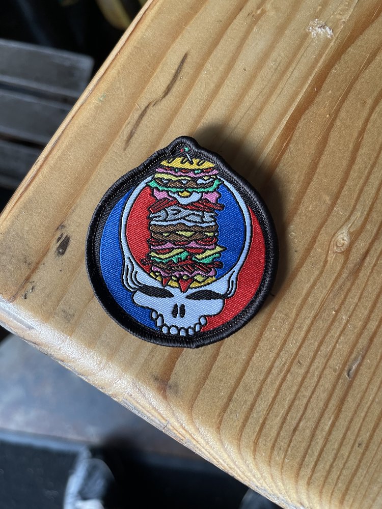 A colourful patch featuring a skull and a sandwich, on a wooden surface.