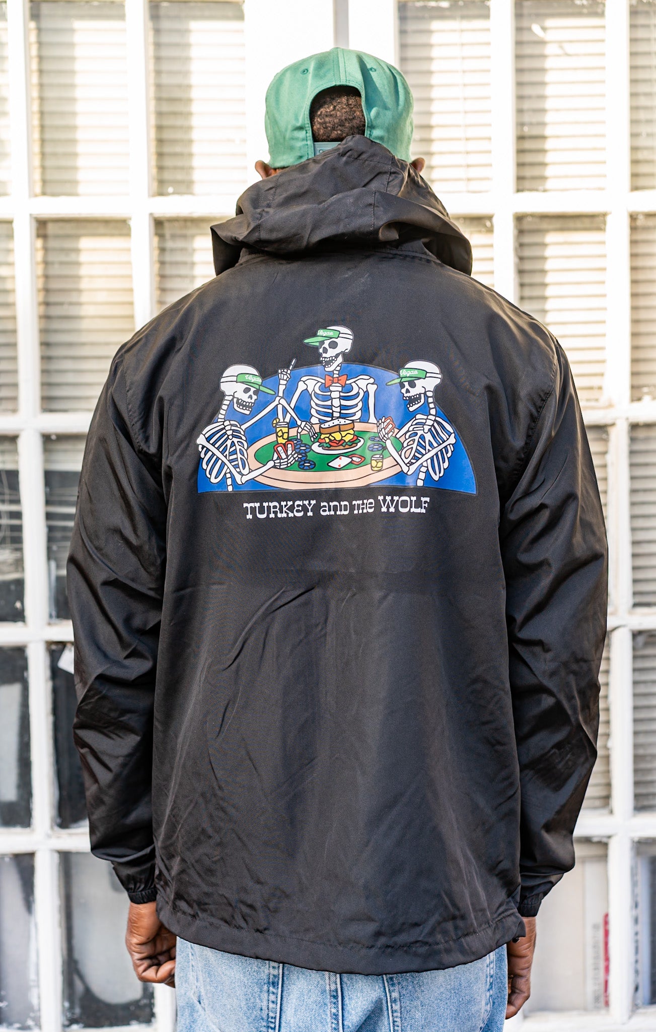 Person wearing a black jacket with a graphic design on the back, standing in front of a window.