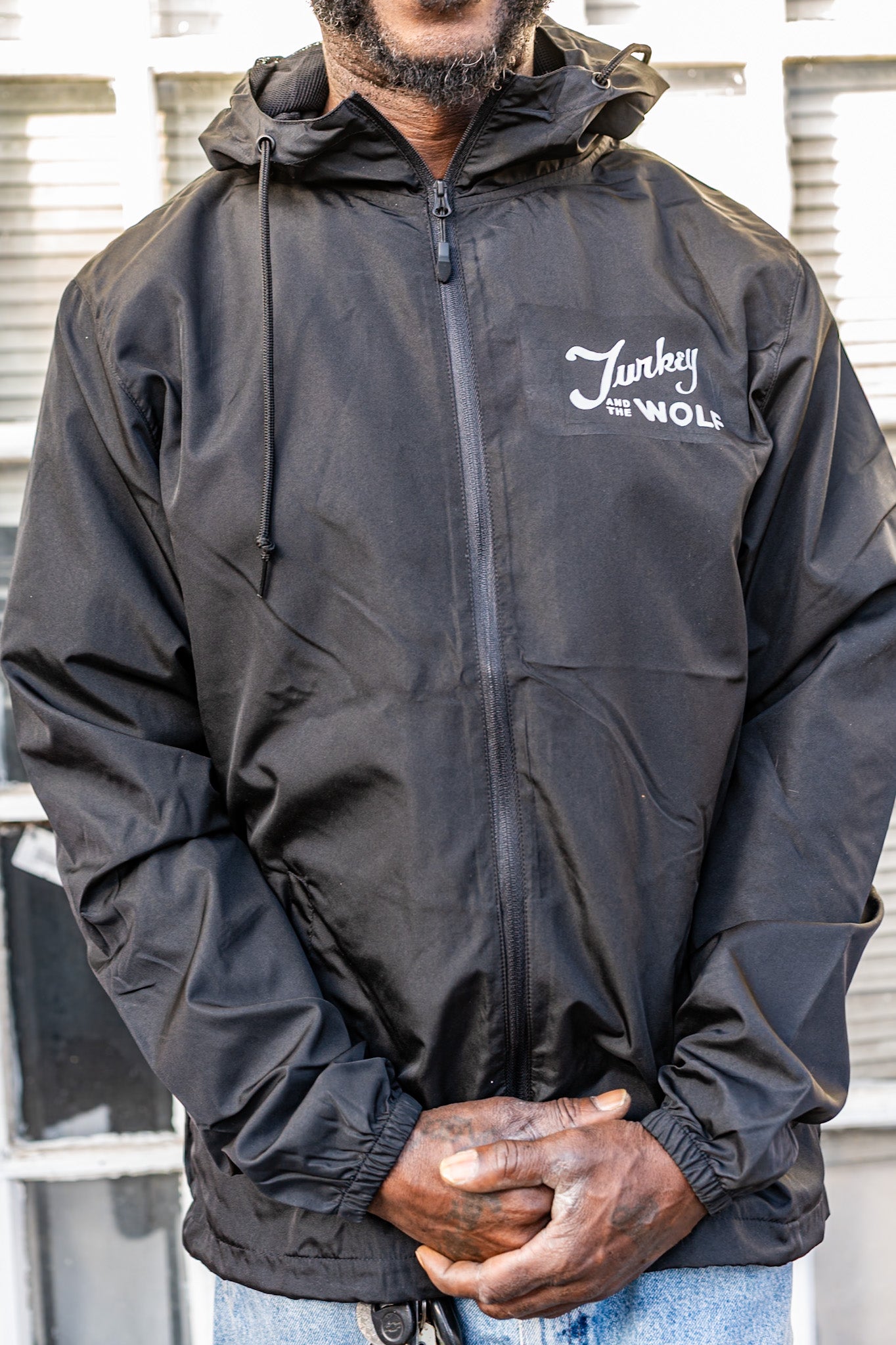 Person wearing a black jacket with a brand logo, standing against a neutral background