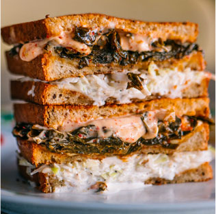 A stacked sandwich with creamy sauce and greens on a floral plate, showcasing its layers.