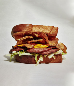 A towering sandwich with crispy bacon, melted cheese, and lettuce on a toasted bun.
