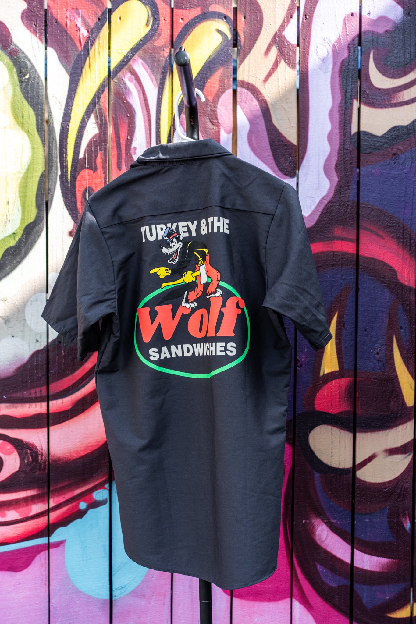 Black shirt with 'Turkey & The Wolf Sandwiches' logo on a colorful mural background
